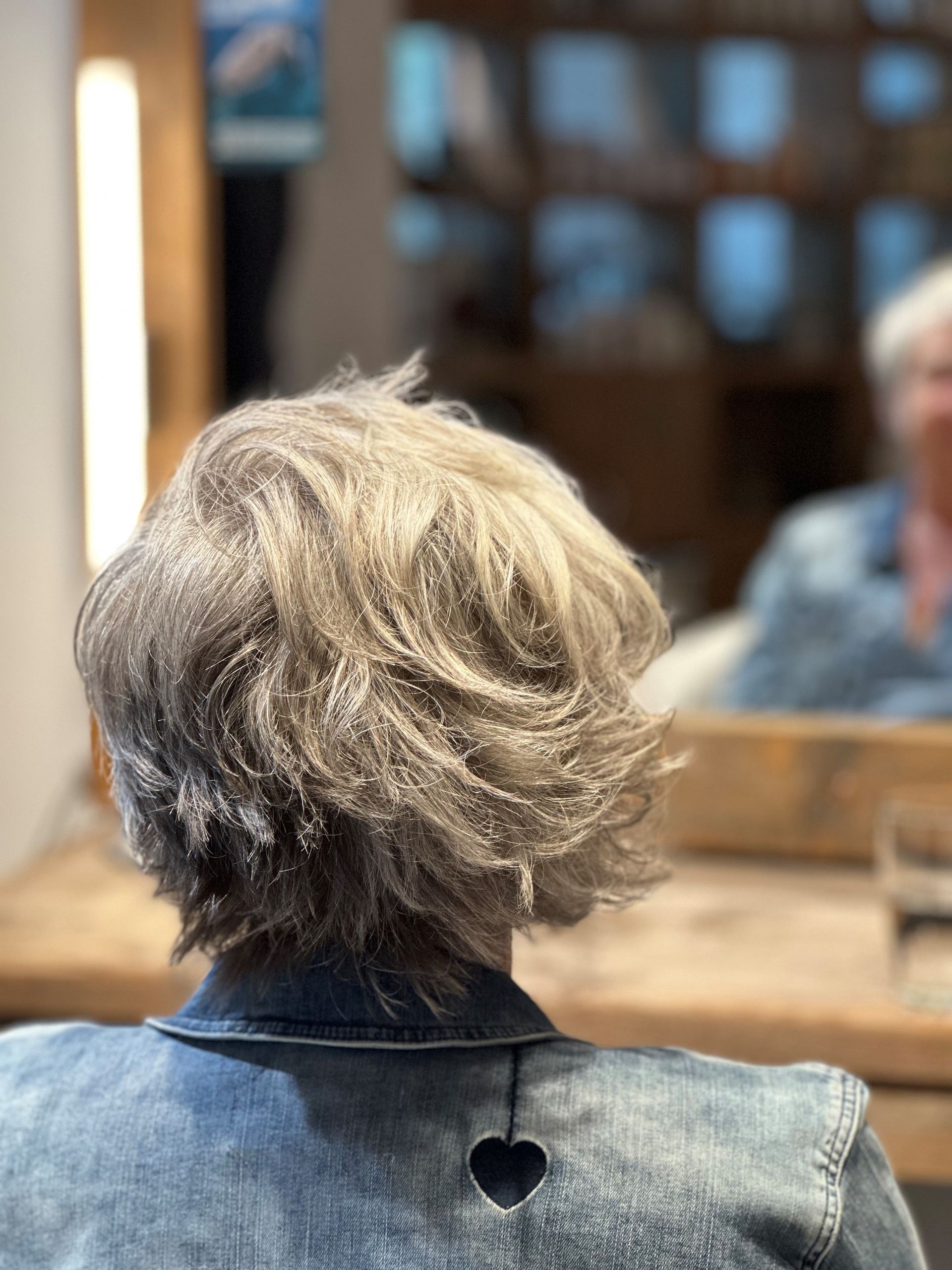 Eine Frau sitzt mit dem Rücken zur Kamera vor einem Spiegel.