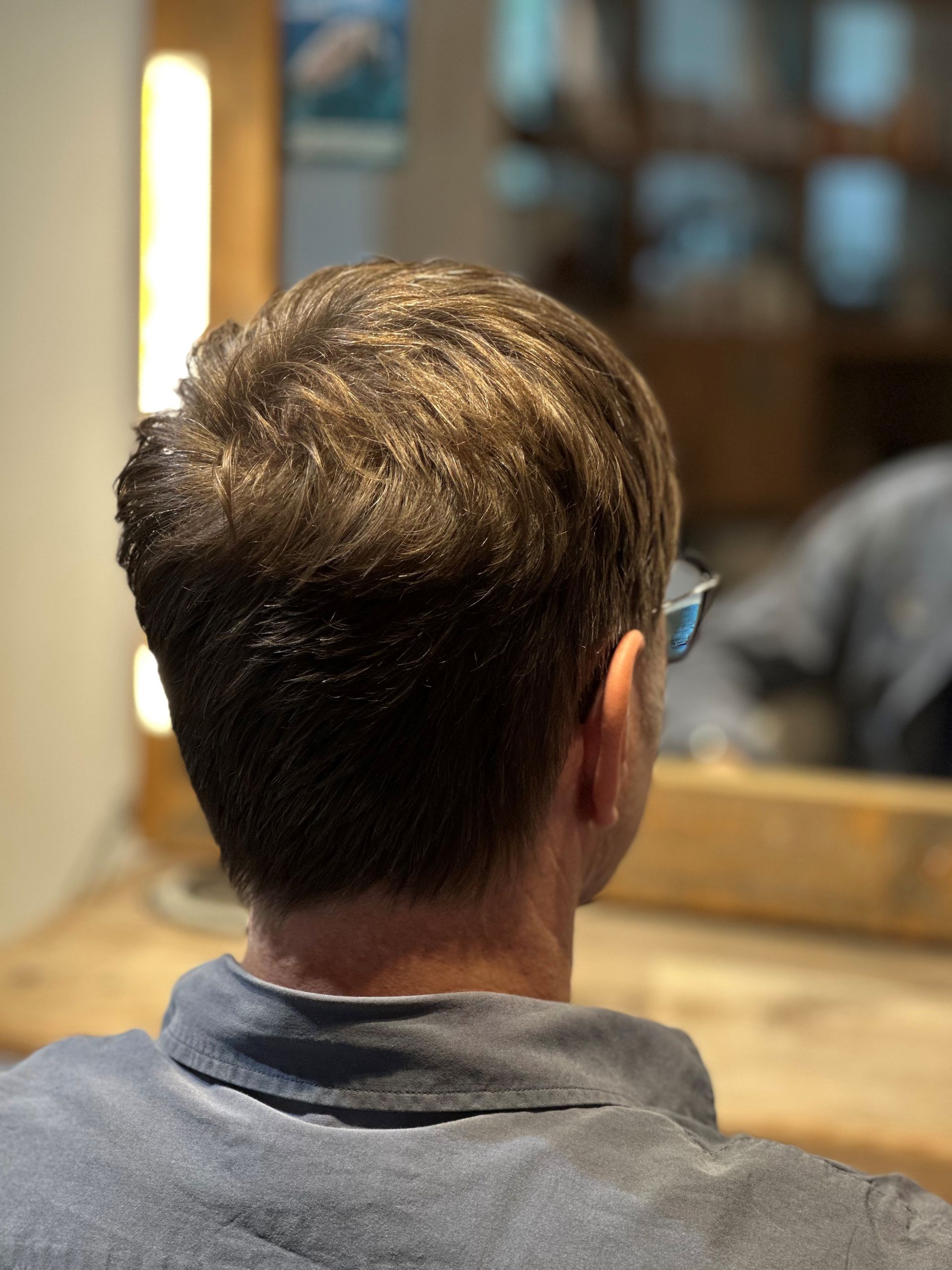 Ein Mann mit Brille sitzt vor einem Spiegel.