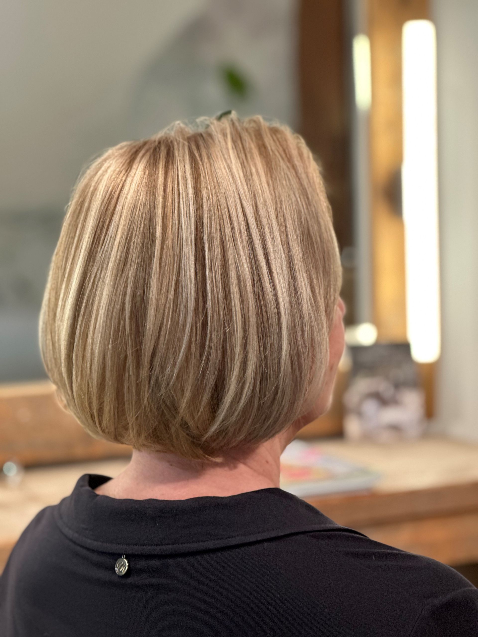 Eine Frau mit kurzen blonden Haaren sitzt vor einem Spiegel.