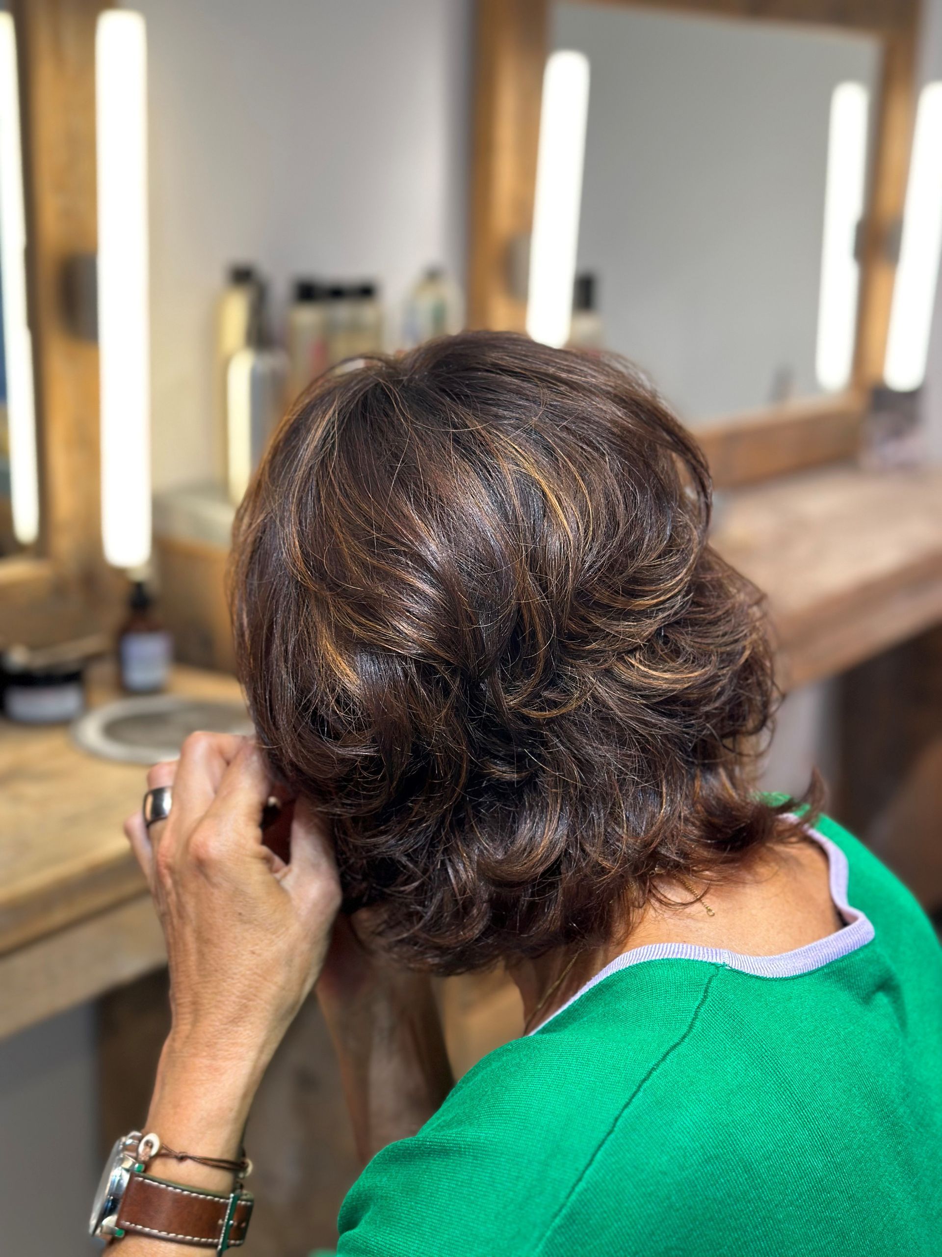 Eine Frau in einem grünen Hemd betrachtet ihr Haar vor einem Spiegel.