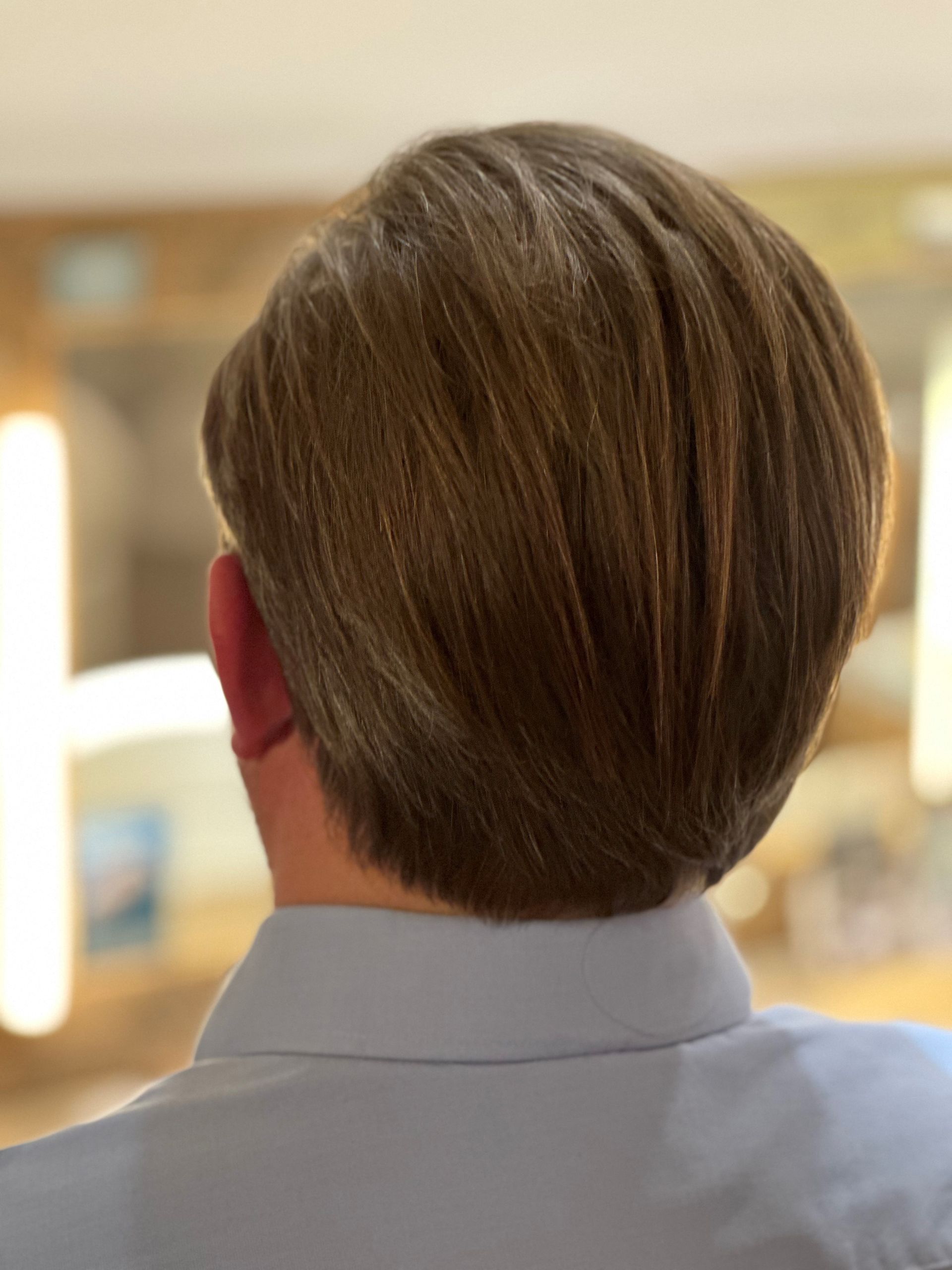 Der Hinterkopf eines Mannes mit kurzen braunen Haaren und einem blauen Hemd.