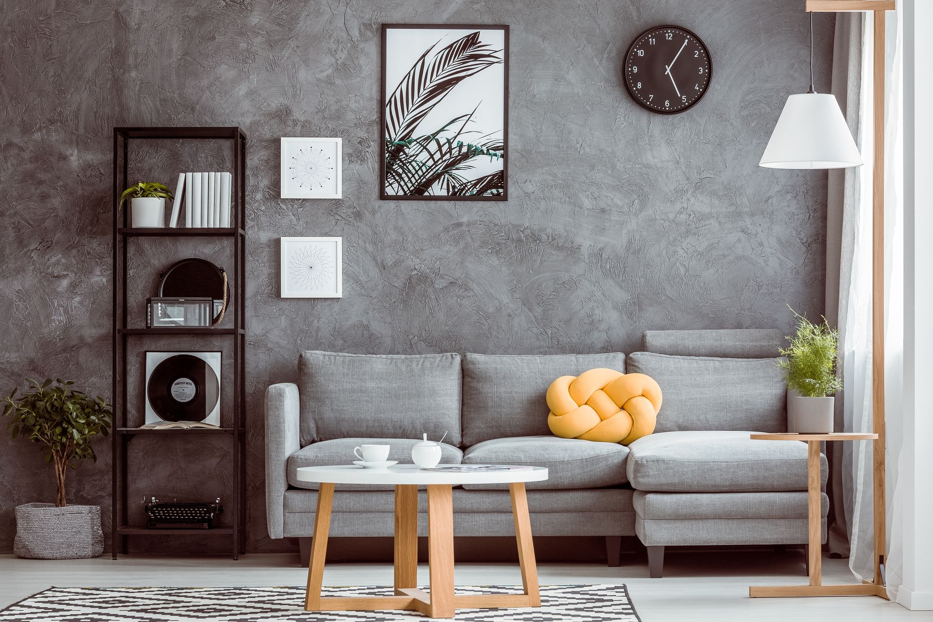 Salon moderne gris avec canapé, table basse, tableau, horloge, étagère et lampe.