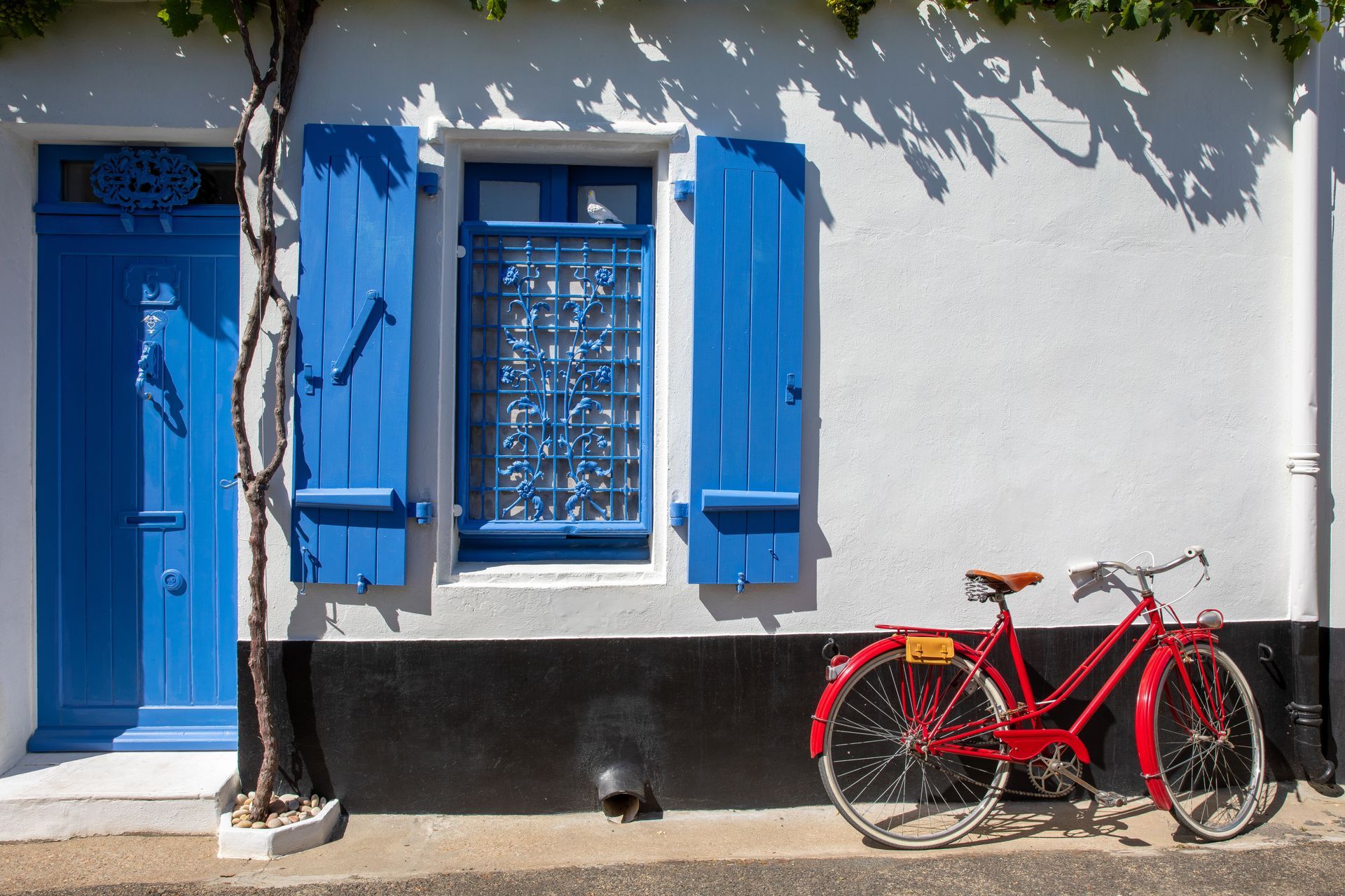 Porte et volets bleus sur une façade blanche, avec un vélo rouge posé contre le mur.