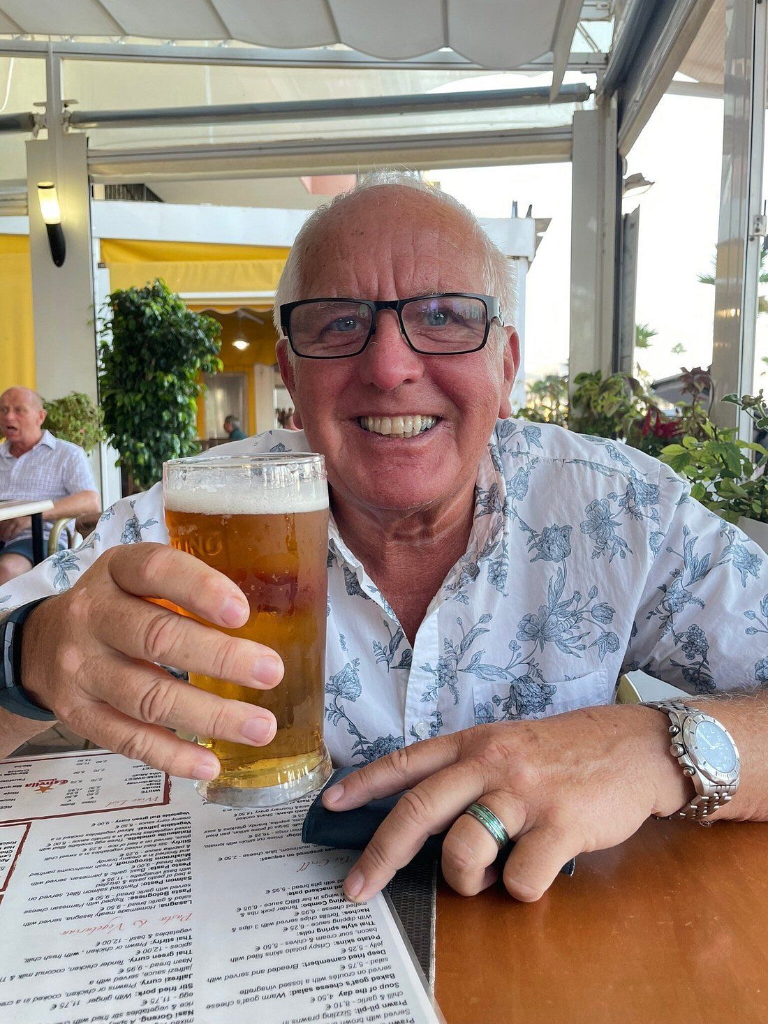 A man is sitting at a table holding a glass of beer.