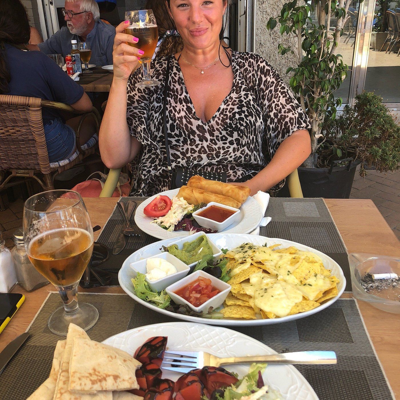 A woman is sitting at a table with plates of food and a glass of beer.