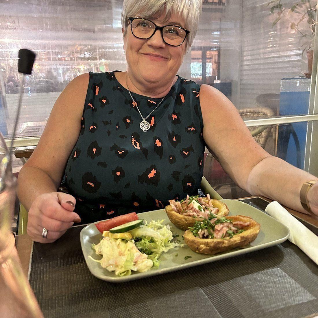 Una mujer está sentada en una mesa con un plato de comida encima.