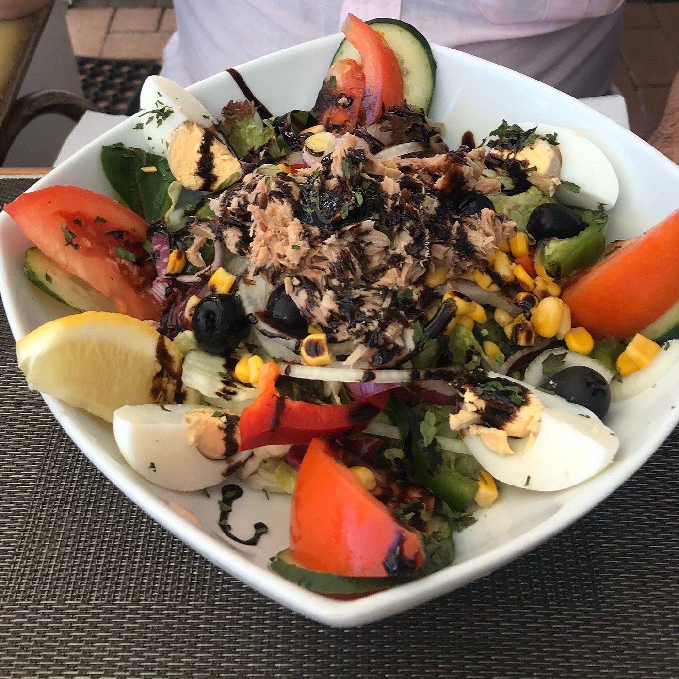 A salad with eggs tomatoes and other vegetables in a white bowl