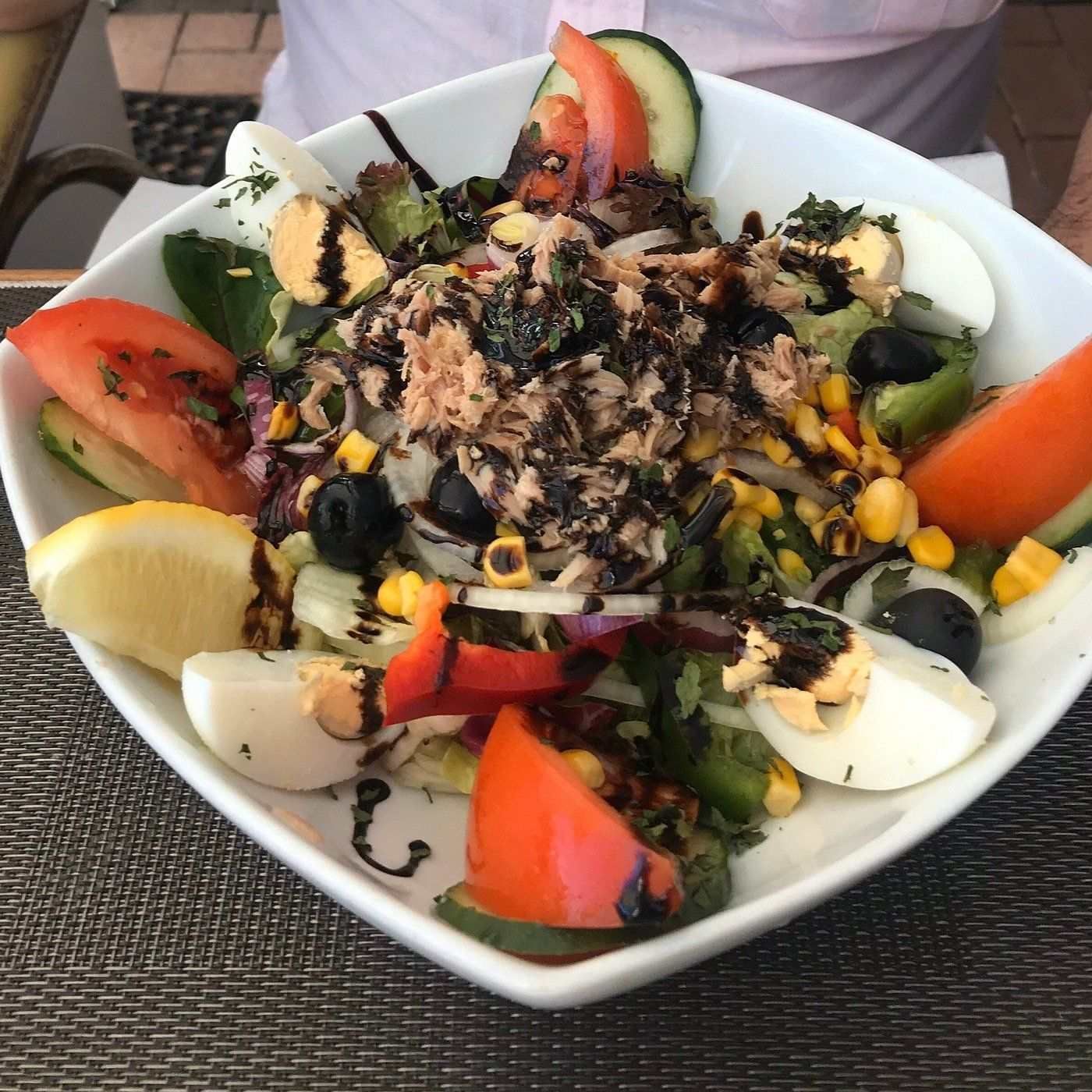 Una ensalada con huevos, tomates y otras verduras en un tazón blanco.