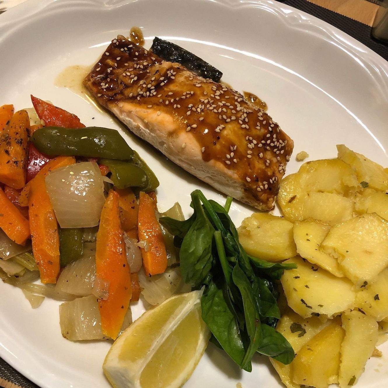 Un plato blanco cubierto con un trozo de salmón, verduras y patatas.