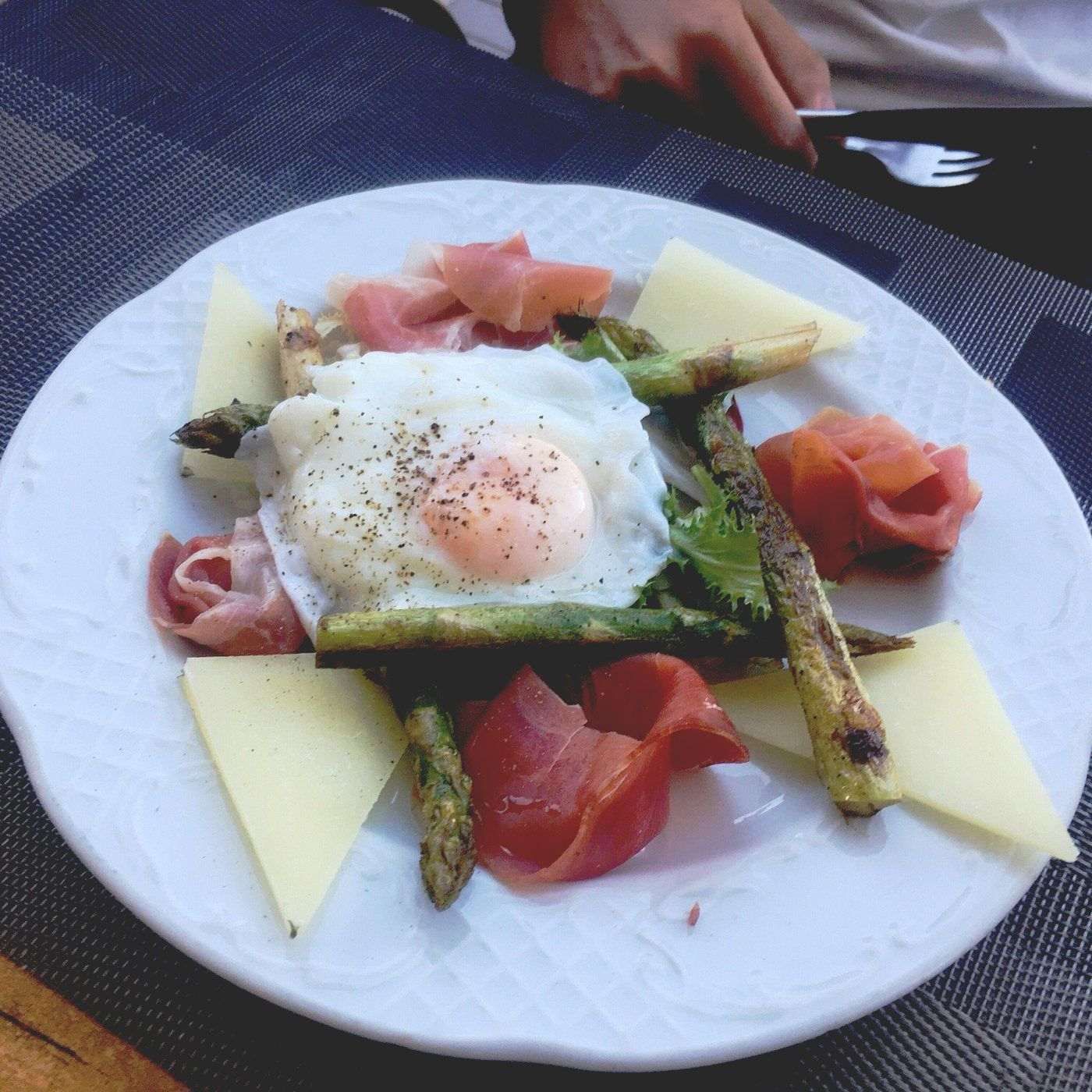 Un plato blanco cubierto con huevos, espárragos, queso y jamón.
