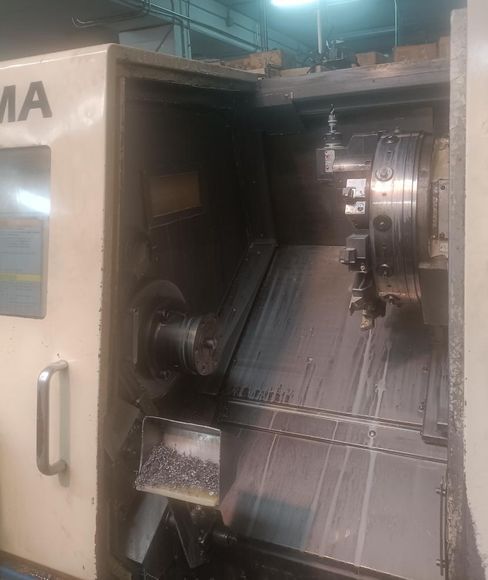 Un torno CNC, con la puerta abierta, mostrando el área de corte y virutas de metal.