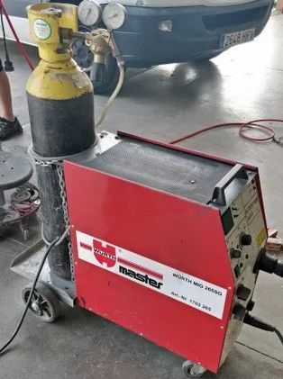 Una máquina de soldar Wurth Master MIG 2100 roja con un cilindro de gas amarillo, una manguera negra y manómetros.