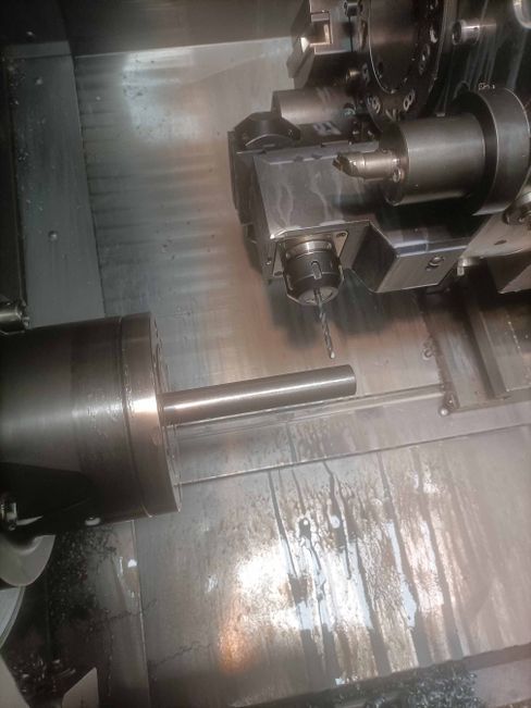 Varilla de metal mecanizada en un torno CNC. Se rocía refrigerante; la máquina está en funcionamiento.