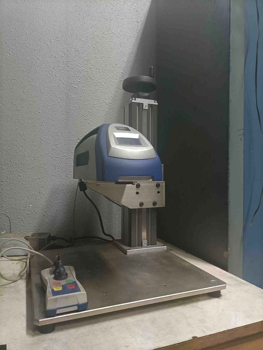 Una máquina con un cuerpo azul y gris, sobre una base de metal con panel de control, en un entorno de laboratorio.