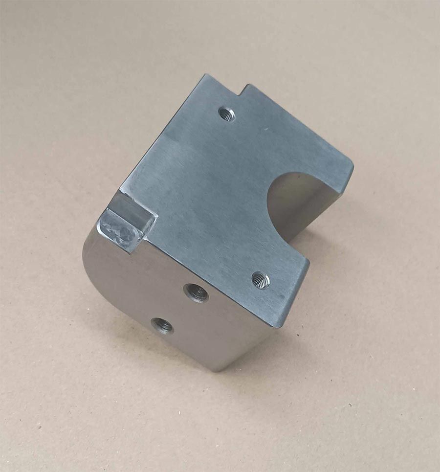 Bloque mecanizado de metal plateado con varios agujeros y sección redondeada.