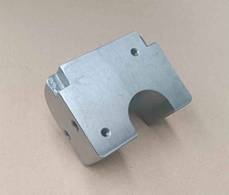 Una pieza de aspecto metálico, de forma rectangular, con un extremo redondeado, varios orificios perforados y un recorte curvo.