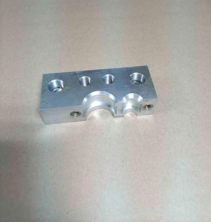 Bloque rectangular de metal plateado con agujeros perforados y recortes curvos.