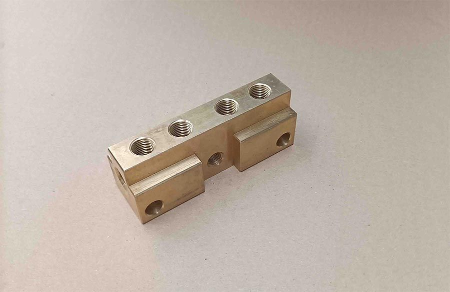 Barra colectora eléctrica de color latón con cuatro orificios roscados en la parte superior y dos orificios de montaje en los laterales.