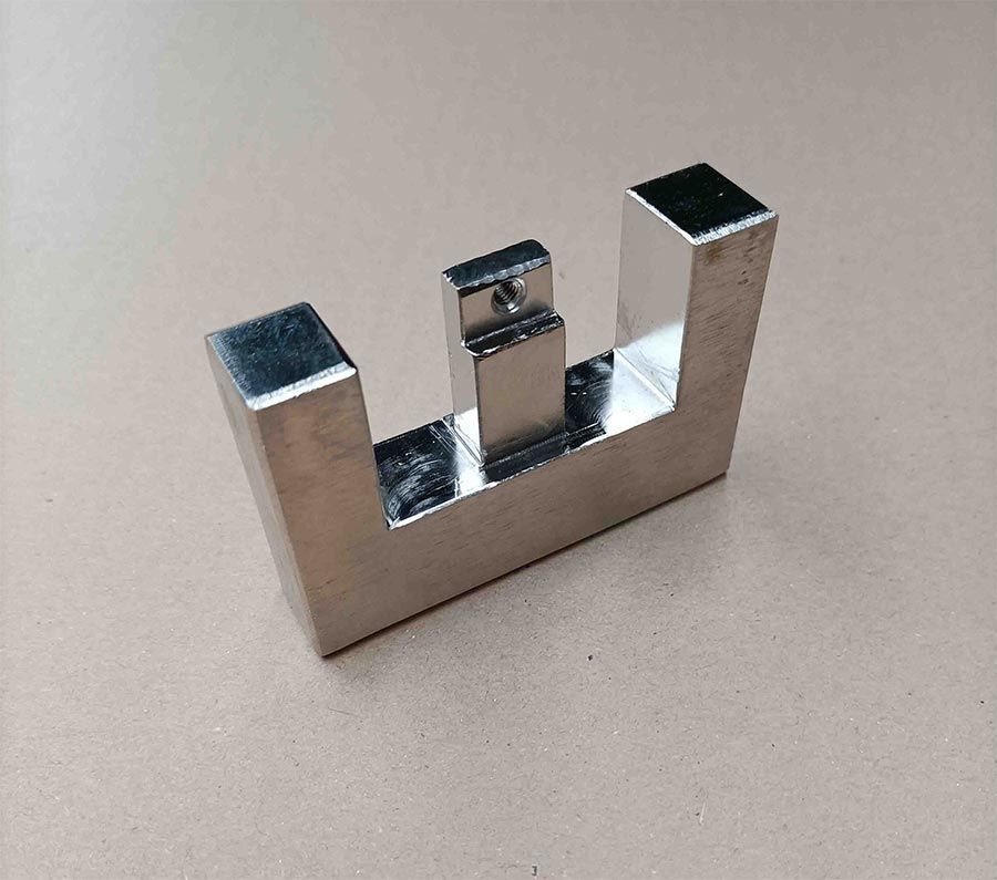 Una pieza de metal brillante, metálica, en forma de U con una pieza más pequeña en la parte superior.