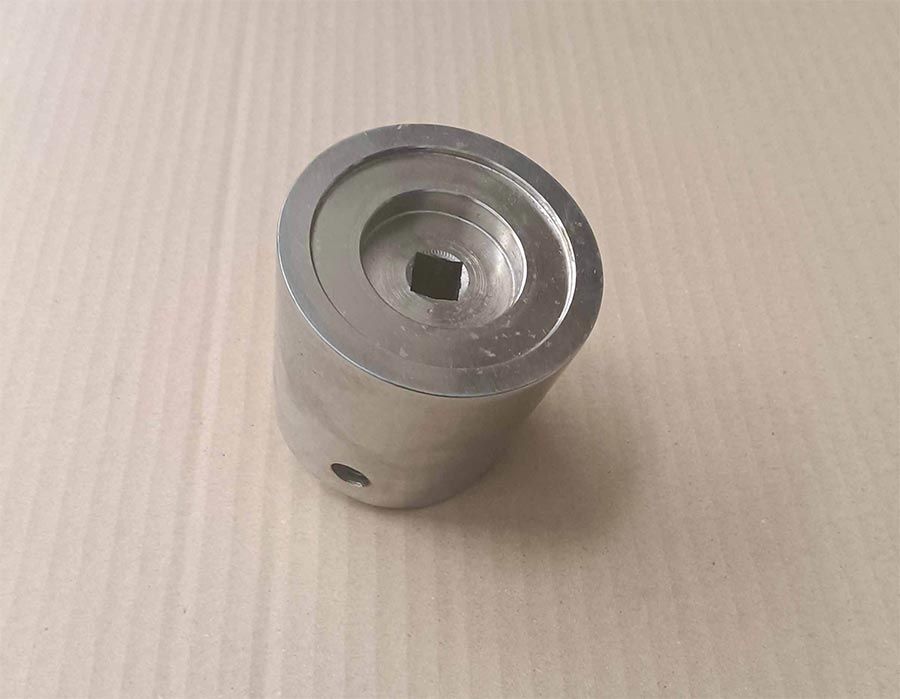 Herramienta de llave de tubo de metal plateado con un orificio cuadrado en el centro, apoyada sobre cartón.