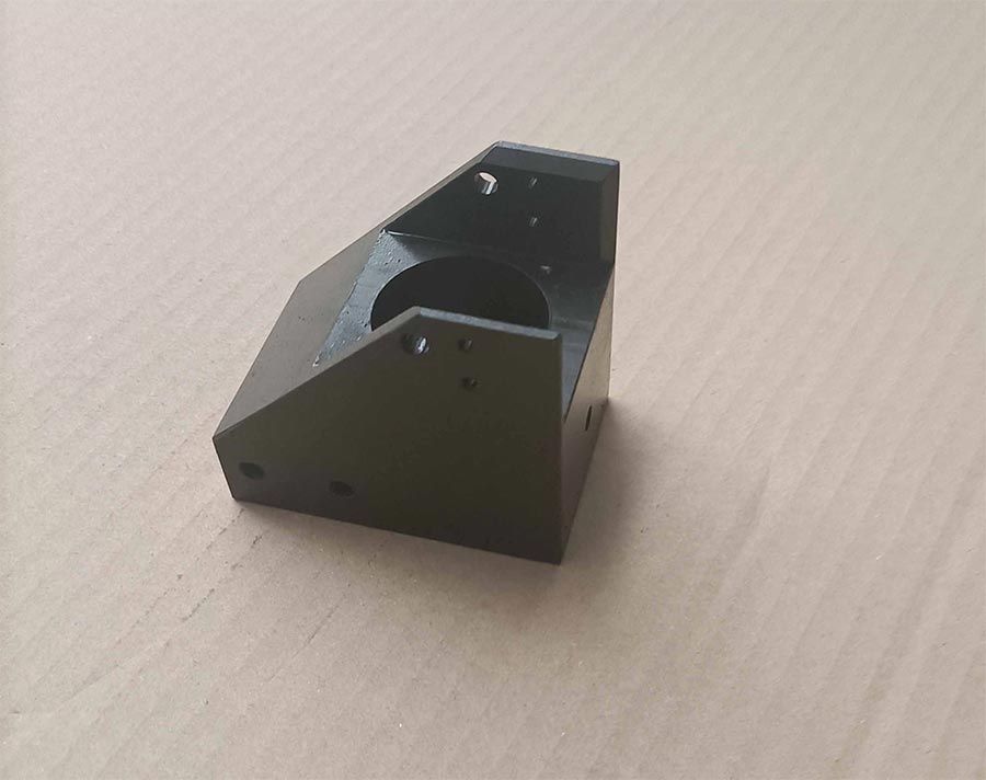 Soporte de plástico negro con un orificio circular, tres lados en ángulo y orificios de montaje.