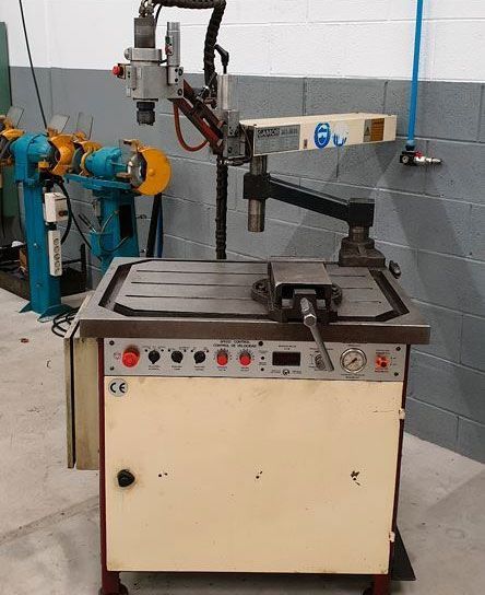 Máquina de soldar industrial con brazo pivotante y tornillo de banco sobre superficie de trabajo.