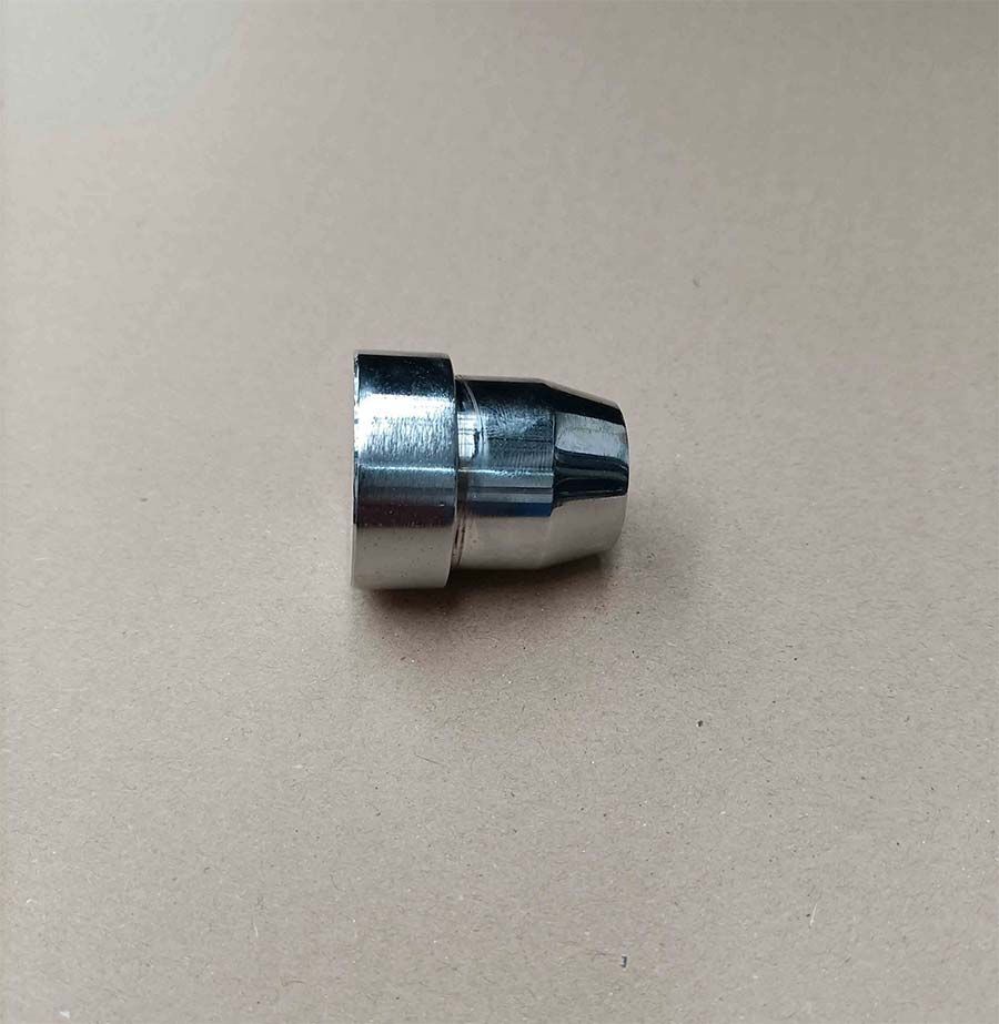 Boquilla de metal plateado con base roscada, sobre superficie marrón.