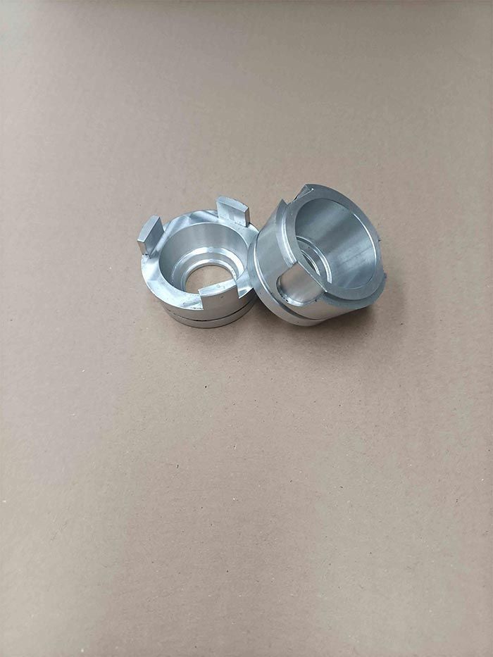 Dos pequeñas piezas metálicas cilíndricas, de color plateado y con el centro abierto, que descansan sobre una superficie marrón.