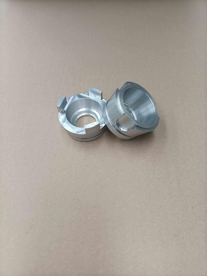 Dos pequeñas piezas de máquina de metal plateado, colocadas sobre una superficie de color beige.