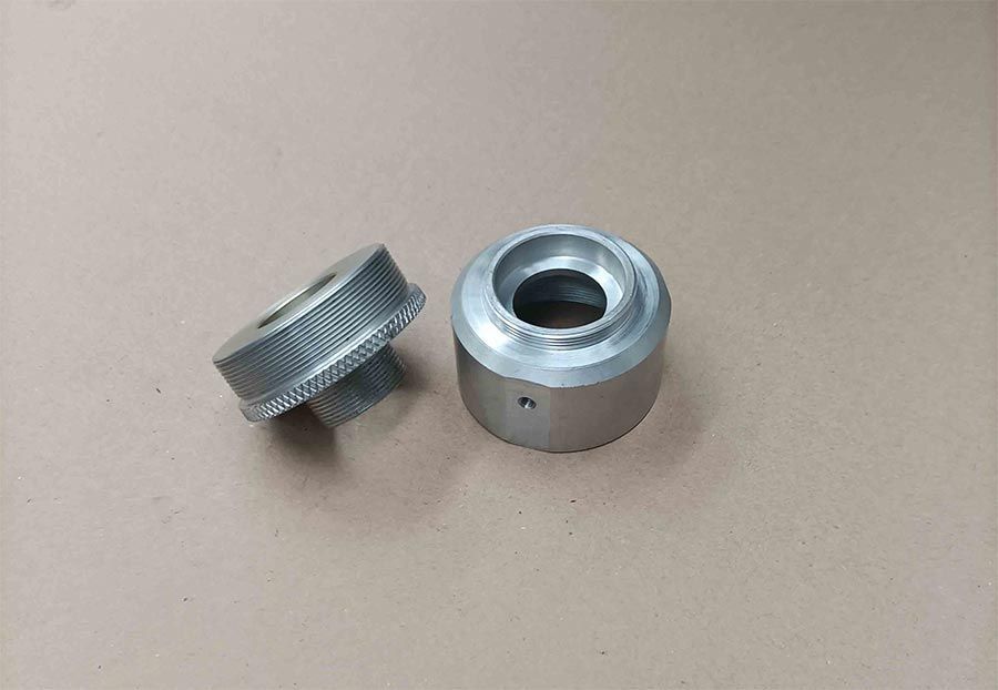 Dos piezas metálicas cilíndricas con borde moleteado y orificio central, sobre fondo neutro.