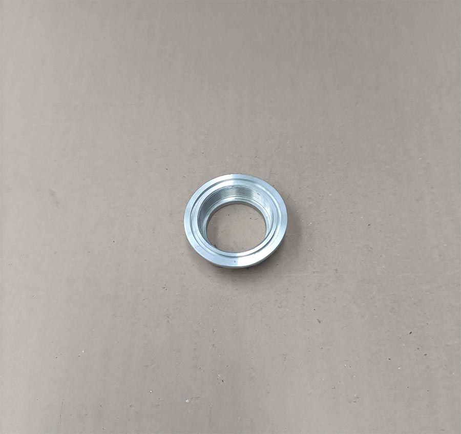 Componente de metal plateado en forma de anillo con un borde interior elevado, centrado sobre una superficie de color canela.