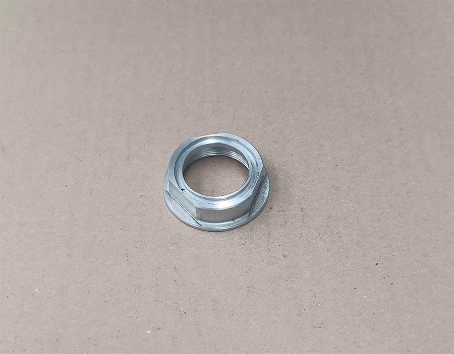 Tuerca de brida metálica hexagonal sobre superficie de tono neutro.