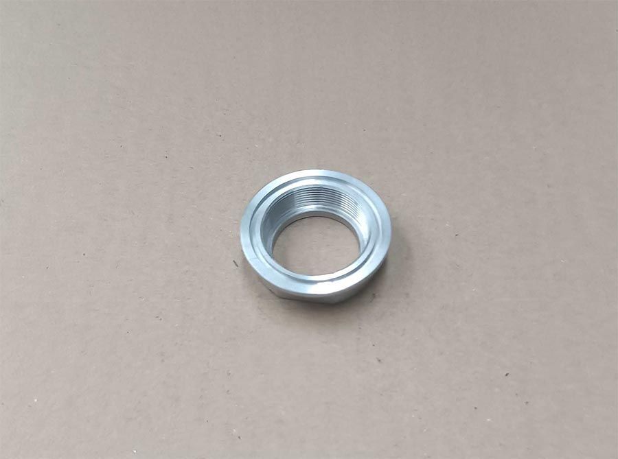 Anillo de metal plateado con orificio interior roscado, sobre superficie de color marrón claro.