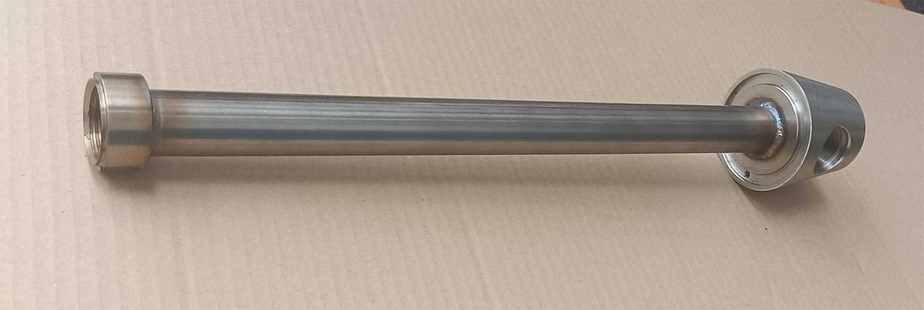 Varilla metálica con extremos roscados y brida, apoyada sobre una superficie de color neutro.