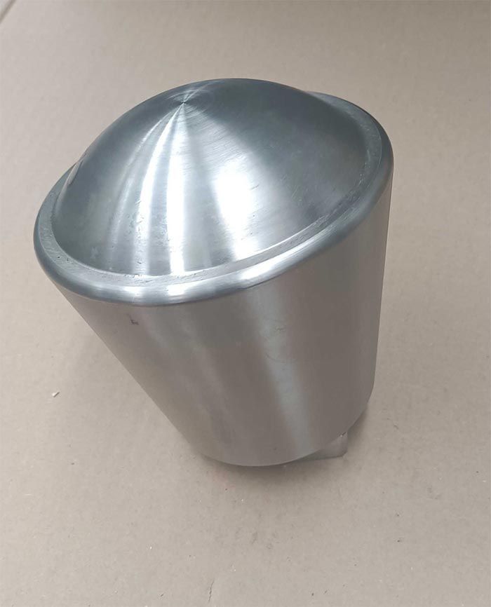 Objeto metálico cónico, anguloso. El objeto es plateado, con superficie lisa y parte superior redondeada.