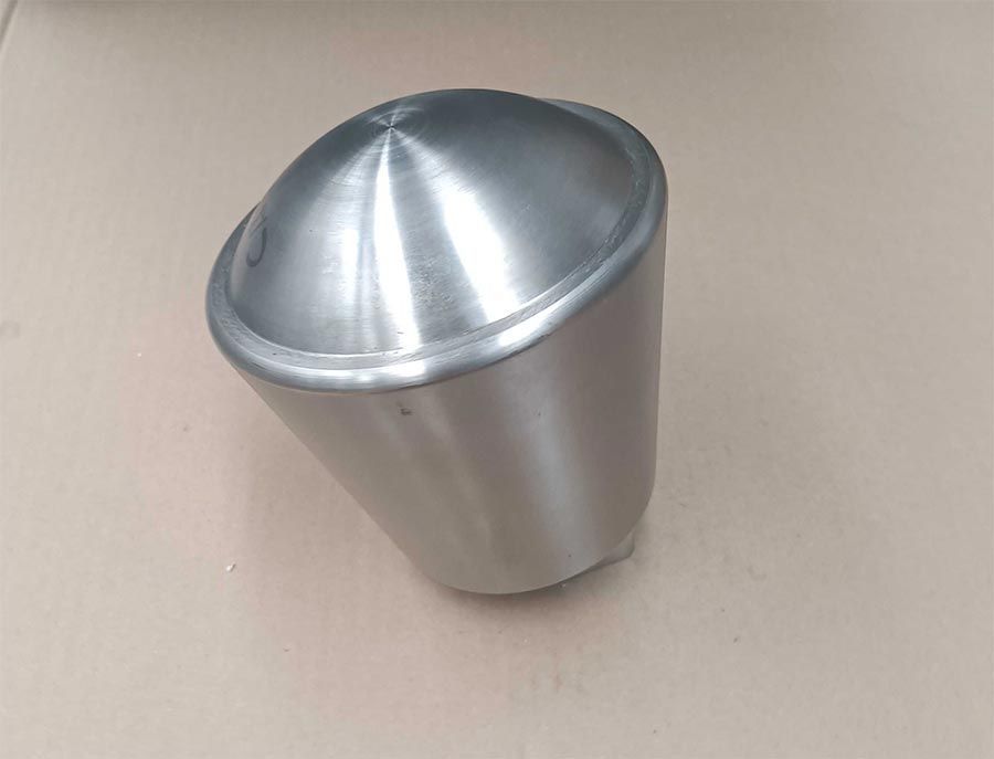 Taza metálica, angulosa, con tapa redondeada, sobre superficie beige.