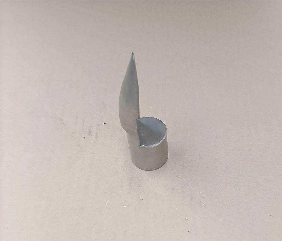 Una herramienta de acero con forma de gancho y base cilíndrica se coloca sobre una superficie neutra.