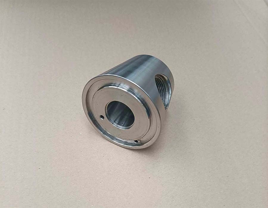 Pieza cilíndrica de metal plateado con agujeros roscados.