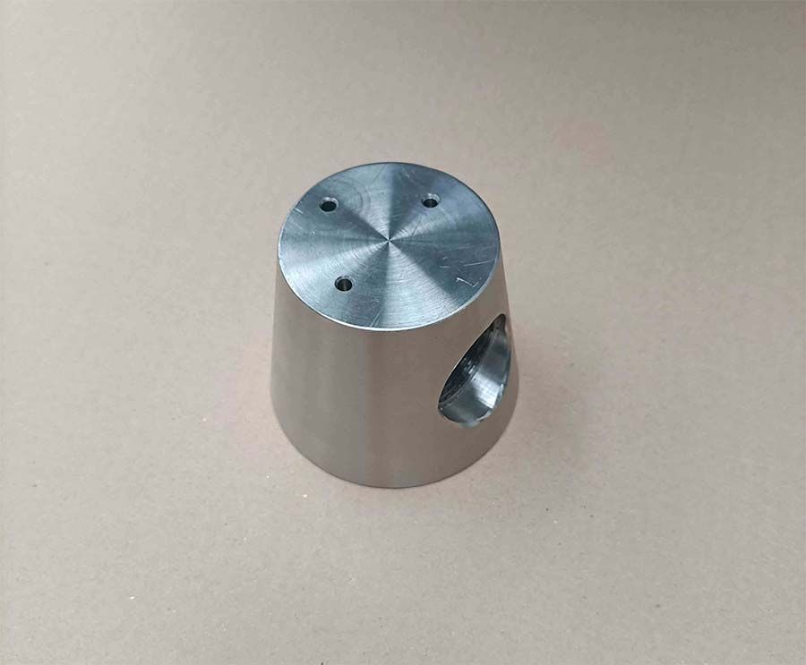 Un objeto cilíndrico de metal con una base ensanchada y tres agujeros en la parte superior y un agujero en el costado.