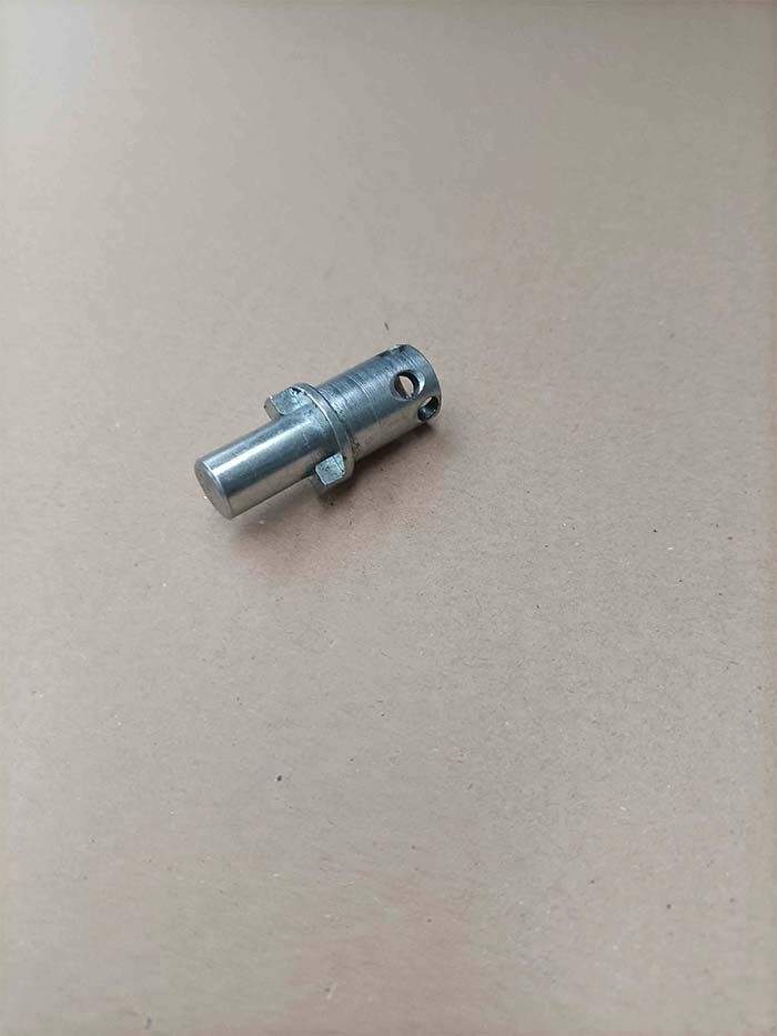 Pasador cilíndrico de metal plateado con un eje pequeño, dos pestañas salientes y dos orificios.