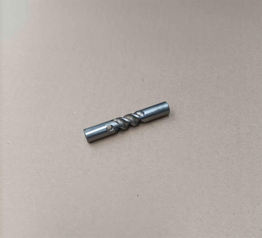 Varilla de metal retorcida con extremos lisos y agujeros, sobre una superficie de color canela.