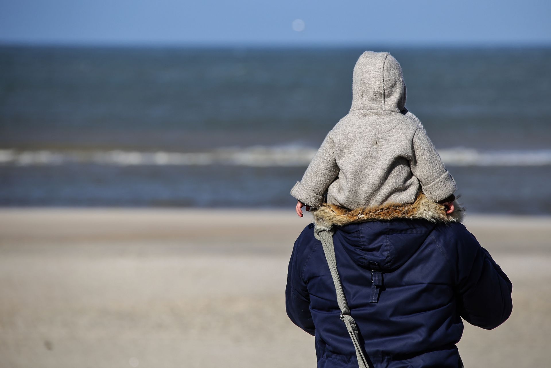 Een vrouw draagt ​​een baby op haar schouders op het strand.
