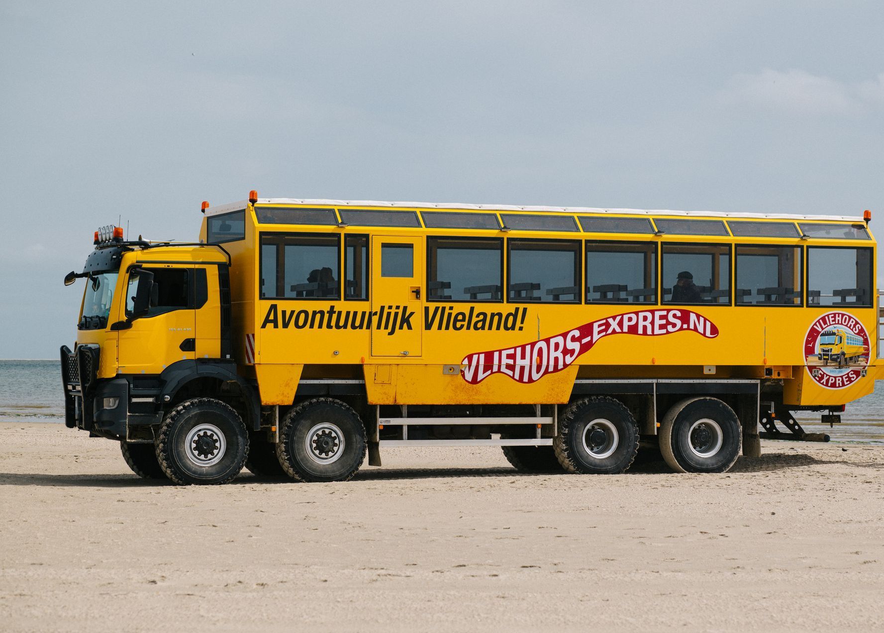 Een gele bus staat geparkeerd op het strand naast de oceaan.