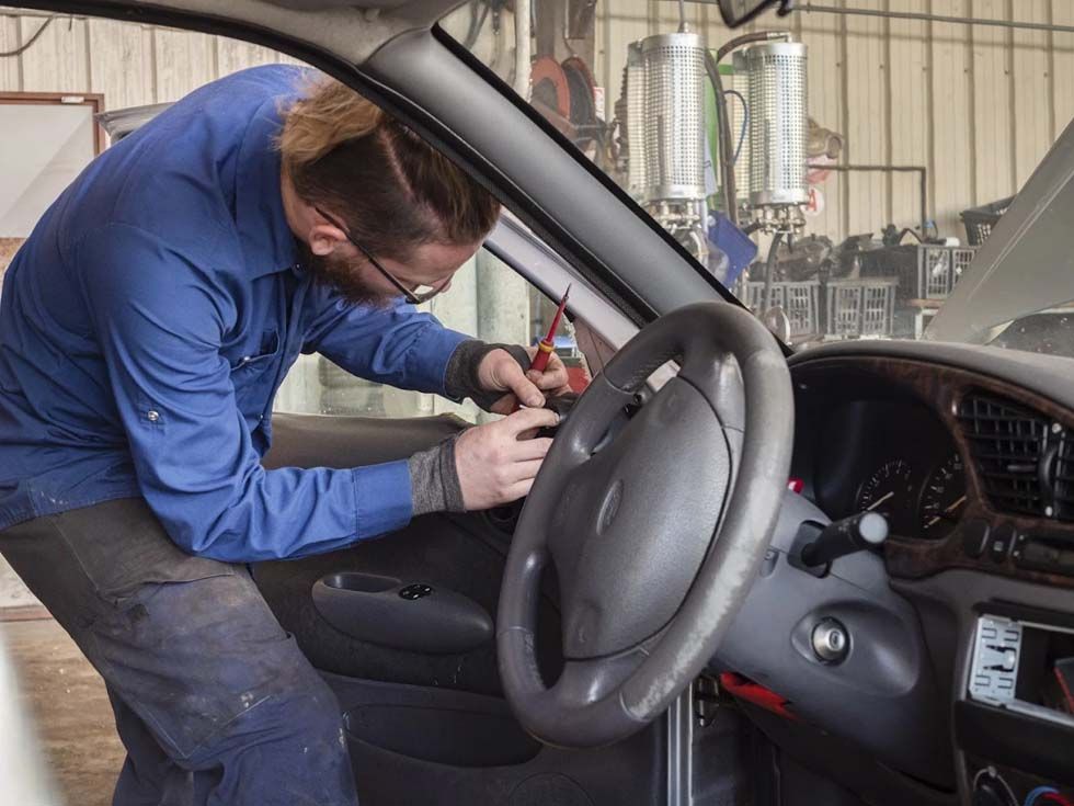 Un mécanicien travaille à l'intérieur du tableau de bord d'une voiture, utilisant un outil près du volant.