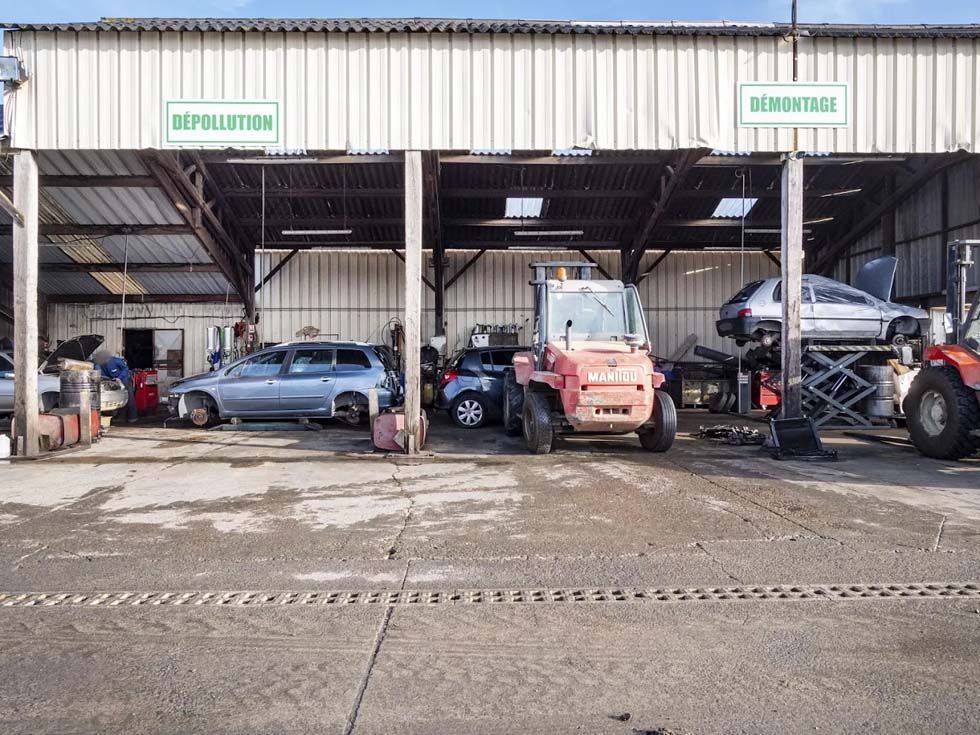 Des véhicules stationnés à l'intérieur d'un garage-entrepôt avec des emplacements ouverts et un parvis boueux