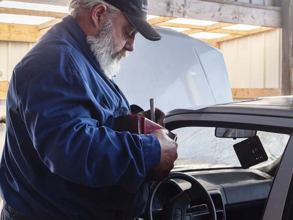 Un mécanicien utilise une perceuse sur le capot d'une voiture dans un atelier.