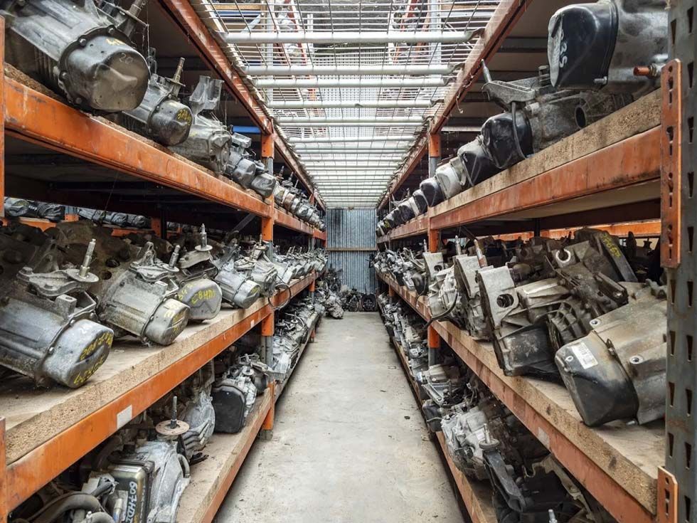 Des rangées de pièces métalliques et de machines sont stockées sur des étagères d'entrepôt dans une longue allée.