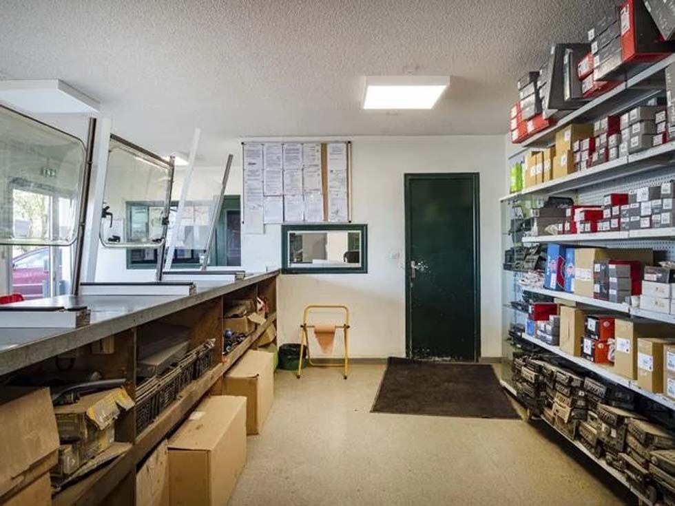 Allée d'un magasin de pièces automobiles avec des étagères de produits, un comptoir à gauche et une porte verte au fond.