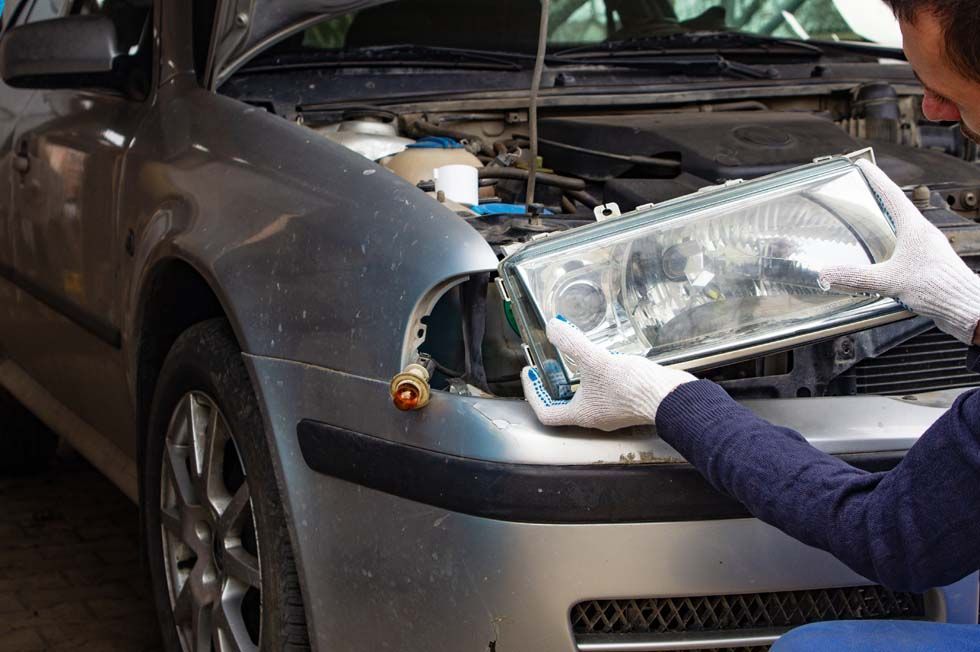 Une personne remplace un phare de voiture à côté d'un véhicule argenté dont le capot est ouvert.