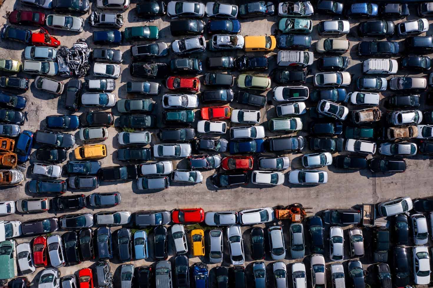 Vue aérienne d'un parking bondé avec des rangées de voitures garées, principalement bleues, grises et noires.